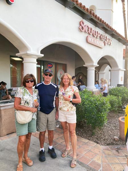 Three people standing outside an ice cream shop named "Scoop and Joy," holding ice cream cones, with others seated in the background.