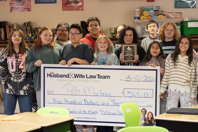 A group of smiling Bellehaven students joins Ms. Martinez in a classroom as they proudly hold a large $500 check and a recognition plaque.