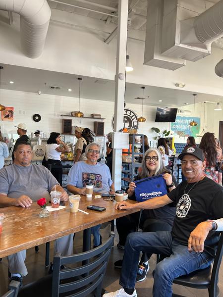 Four friends smile around a wooden table at Collective Coffee, drinks in hand