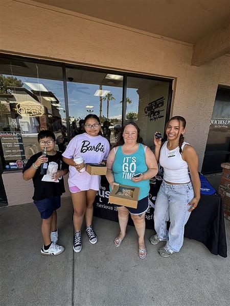 Four attendees smile outside Quiches & Pies Bakery while enjoying pastries and refreshments during a Husband & Wife Law Team HEART event, celebrating community and connection.
