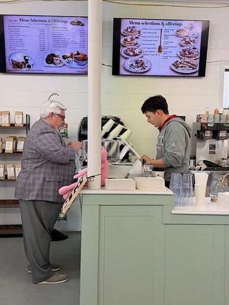 A Milk and Honey Caffe customer chats with the barista at the counter, framed by glowing menu screens and coffee