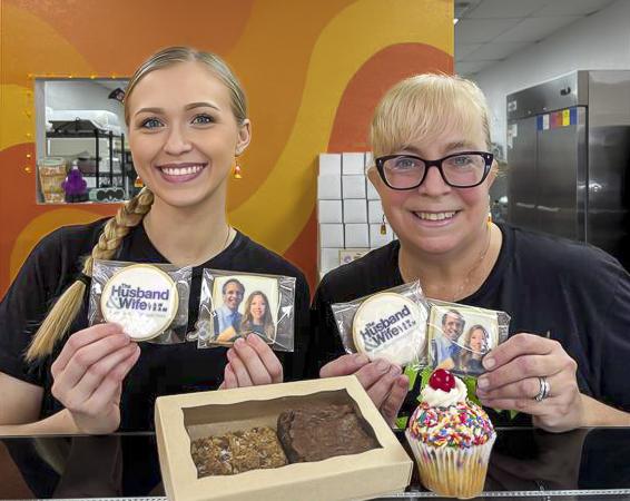 Two smiling Besties Bakeshop team members show off custom cookies and sweet treats during the Husband & Wife Law Team’s HEART event.