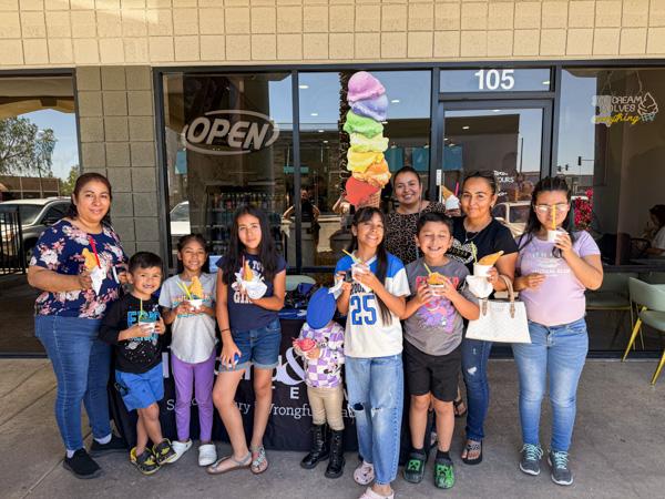 Families and community members smile outside Iced Out Ice Cream, holding colorful cones in hand.