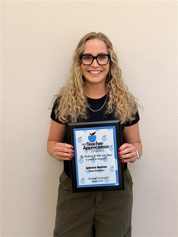 Mrs. Benton smiles, holding a framed Teacher Appreciation certificate against a plain wall.