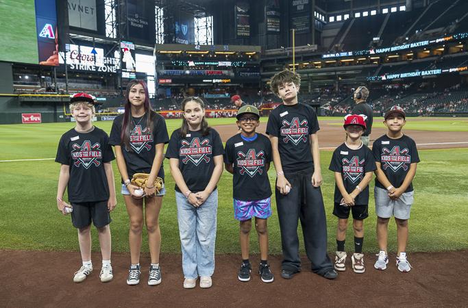 Living the baseball dream! Seven Kids Take the Field winners pose together on the diamond in shirts sponsored by The Husband & Wife Law Team.